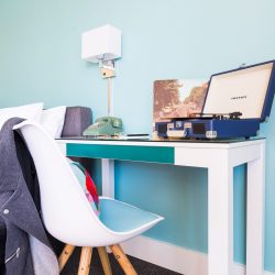 Rambler: desk with blue record player on it and chair with leather jacket draped over it