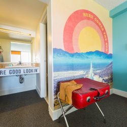 Rambler: view of room sink and red leather suitcase in front of Here Comes the Sun wall graphic