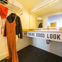 View of sink with Hey There Good Looking artwork and clothes hanging