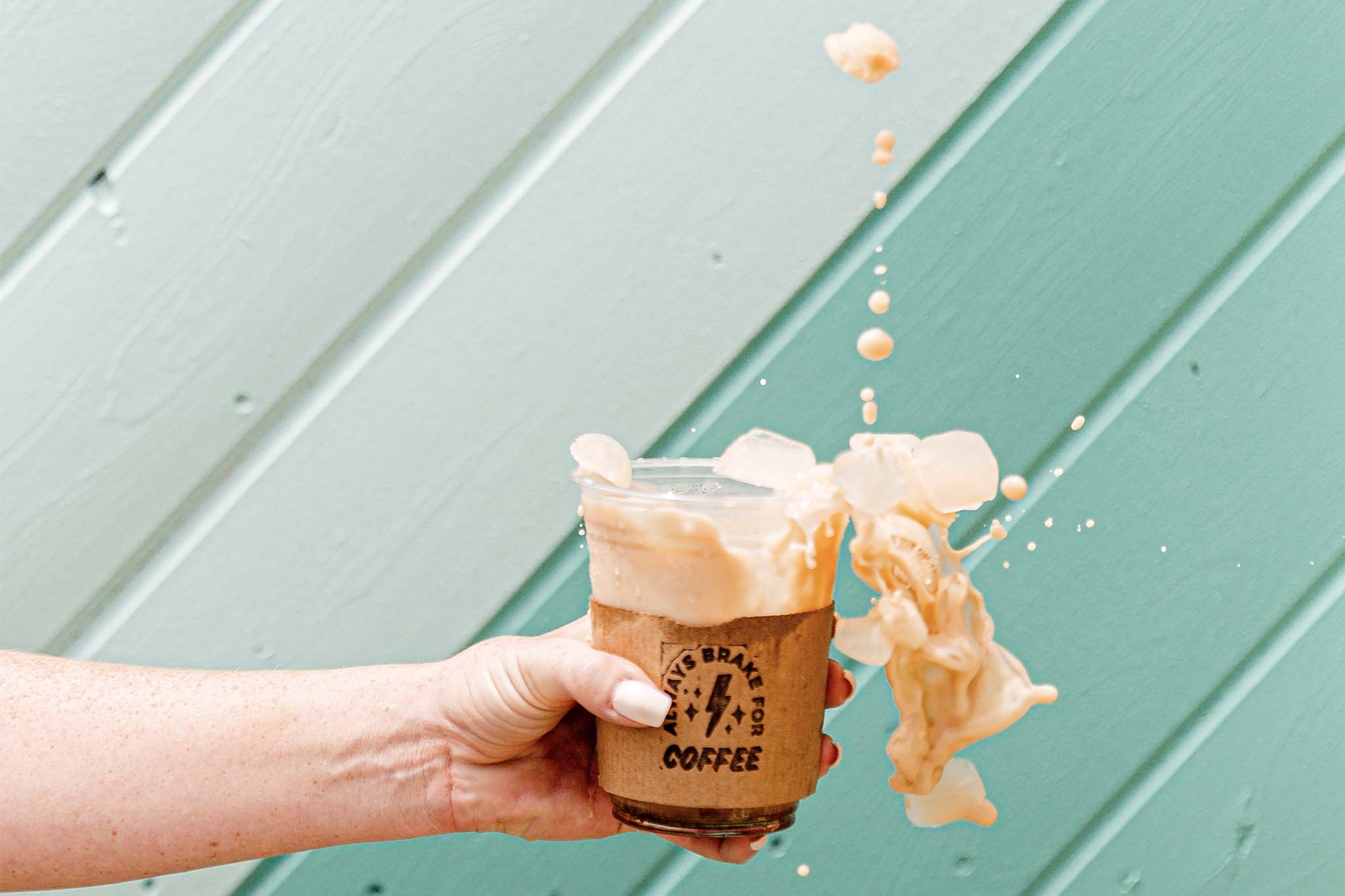 Hand holding a To Go cup of iced coffee that's splashing out of the cup