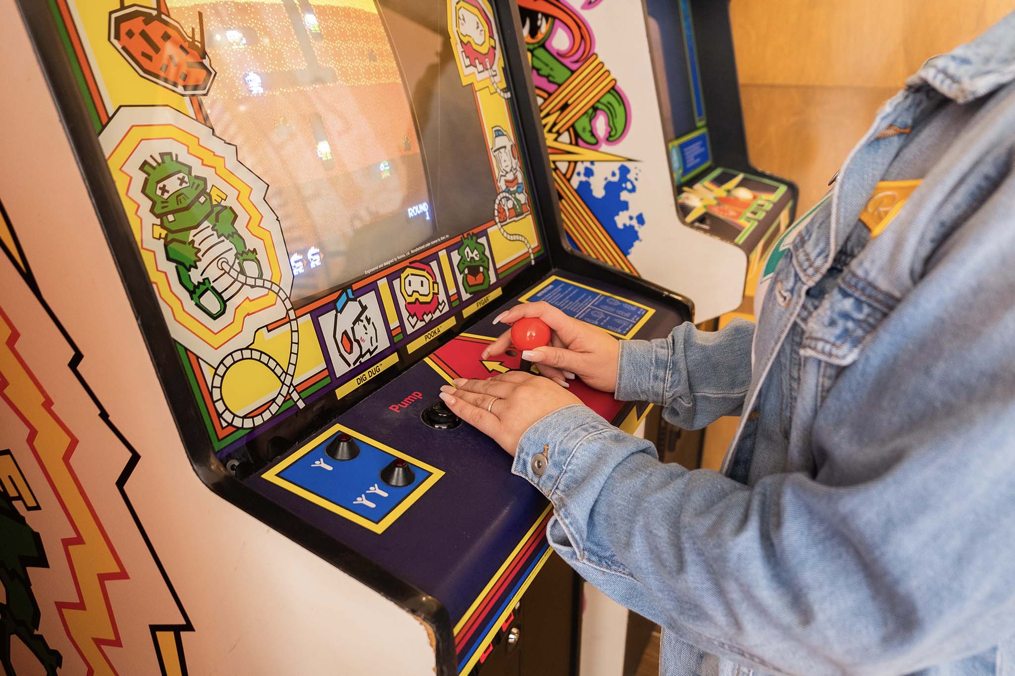 View of hands of a girl wearing a demin jacket playing an old school arcade game