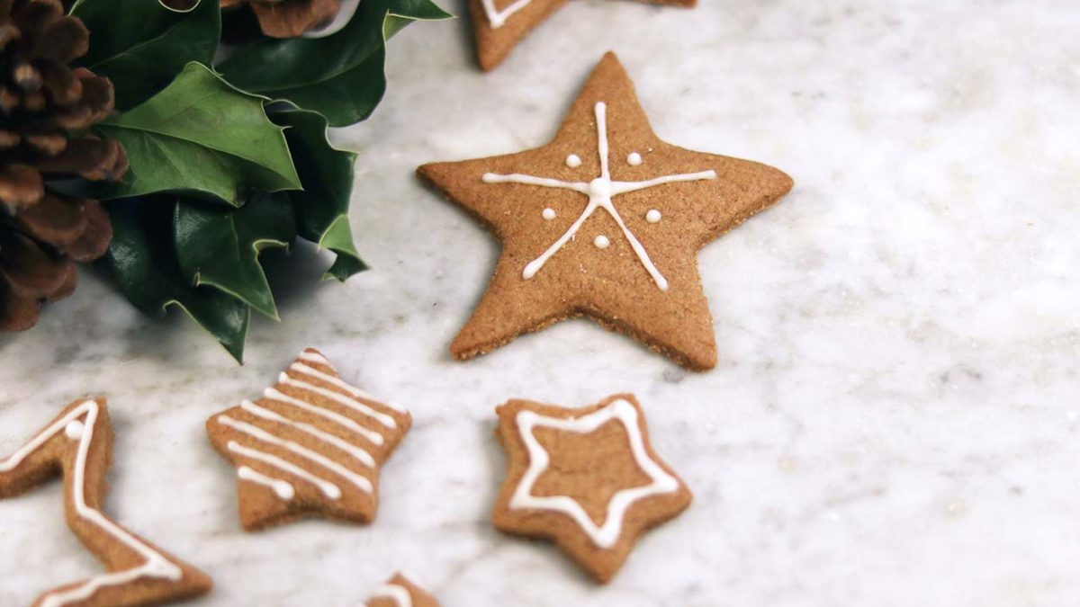 Christmas ginger snap cookies in different star shapes decorated in icing sitting next to holly and pine cones