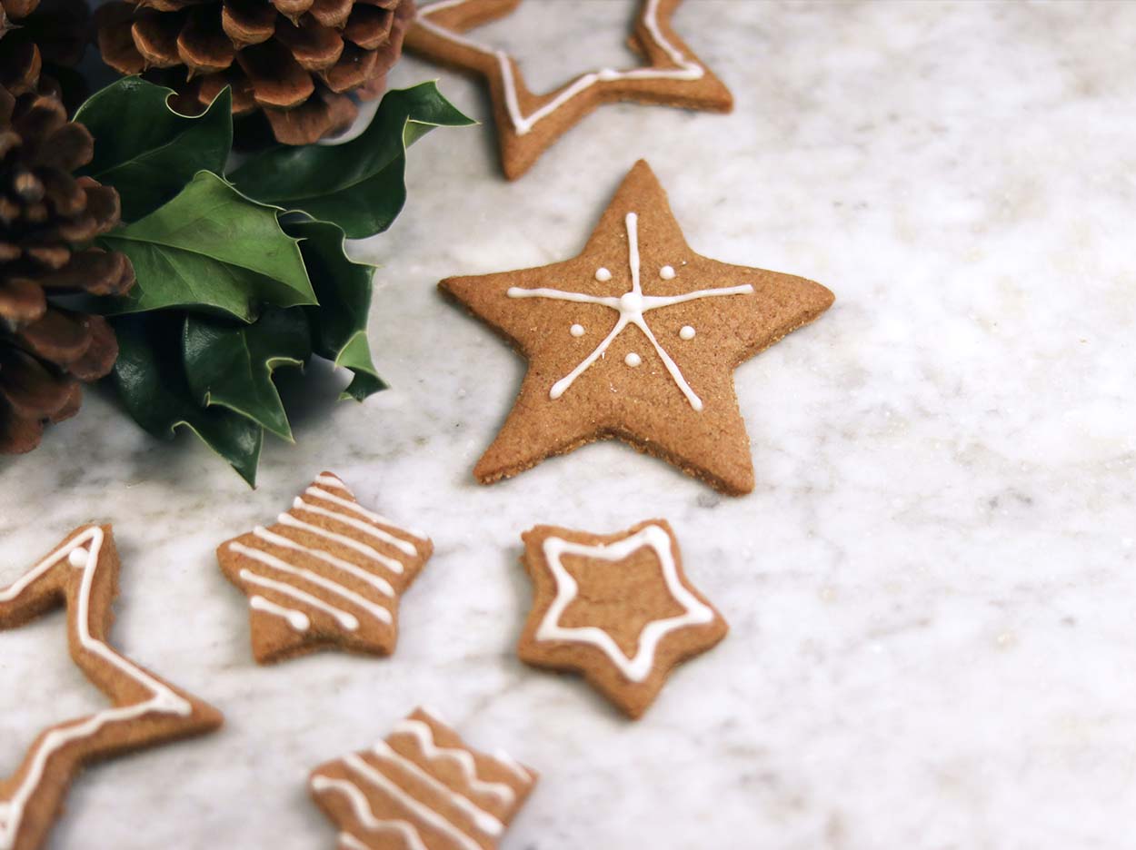 Christmas ginger snap cookies in different star shapes decorated in icing sitting next to holly and pine cones