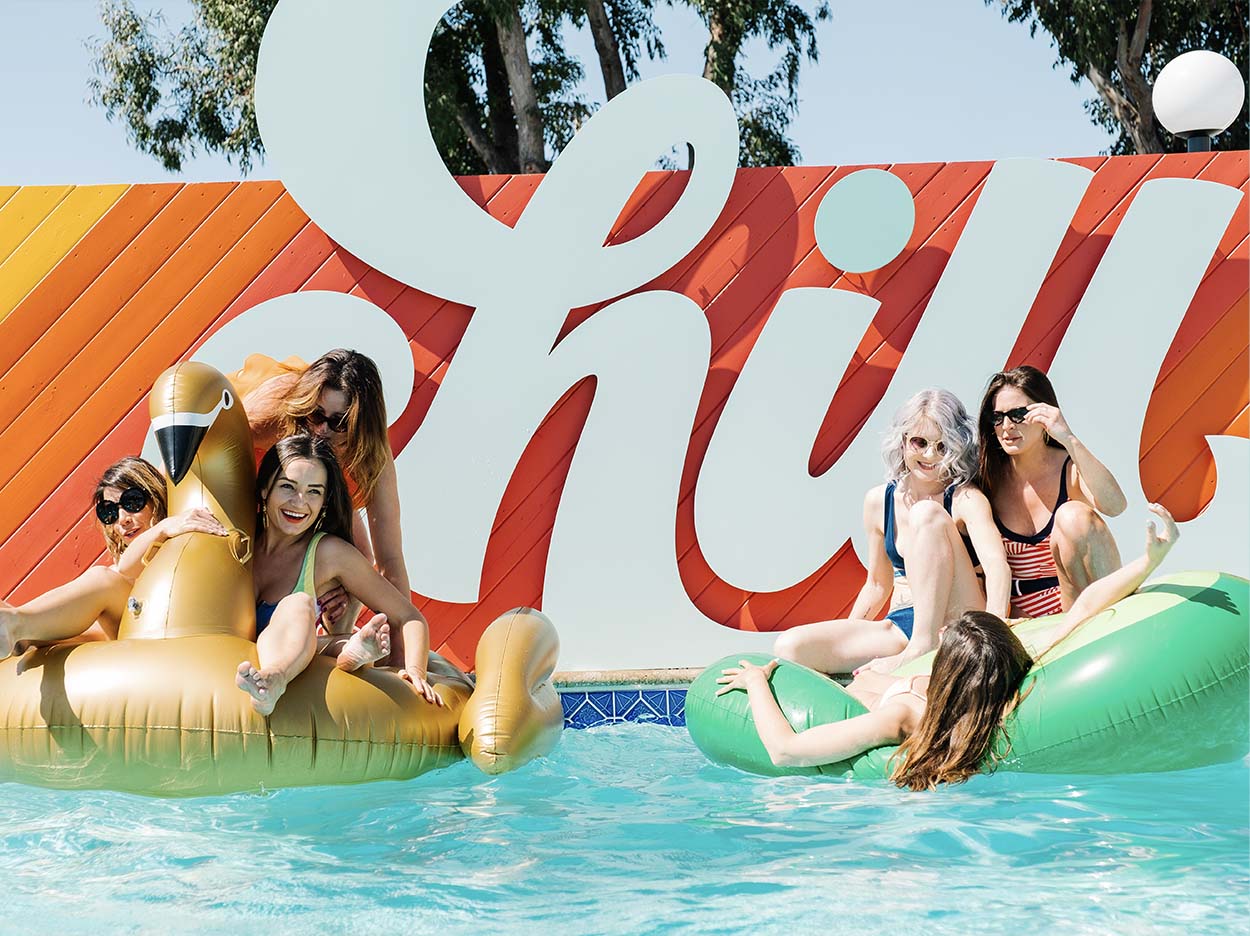 Girls on rafts floating in the Rambler pool in front of the colorful CHILL sign